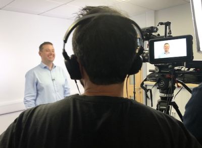 A smiling man being filmed by a professional sound and camera crew